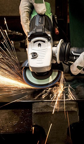 Worker using an industrial grinder on metal, with sparks flying, depicting active metal fabrication.